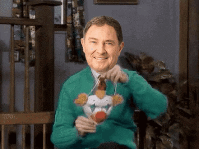 a man wearing a green sweater with a clown on it is smiling