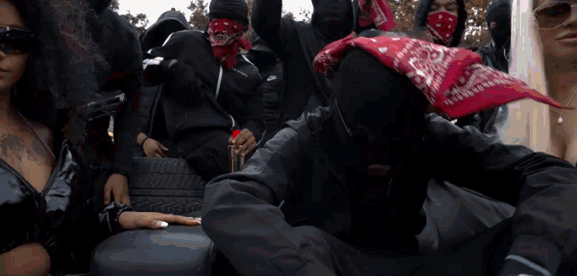 a man wearing a red bandana covering his face points at the camera
