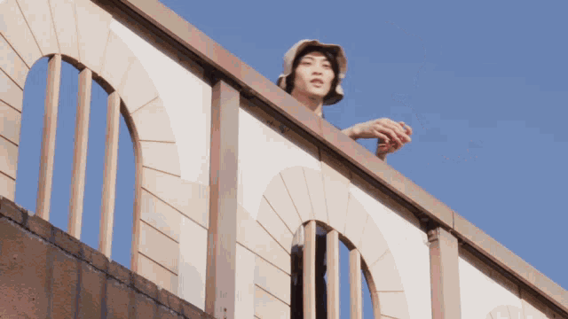 a person wearing a hat stands on a balcony