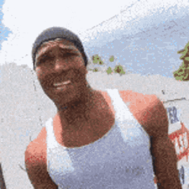 a man wearing a hat and a white tank top smiles