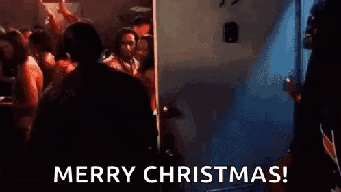 a man in a suit is standing in front of a crowd of people in a room and saying merry christmas .