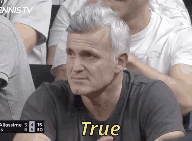 a man sitting in a crowd with the word true written on his shirt