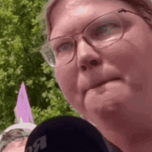 a woman wearing glasses is talking into a microphone and making a face .