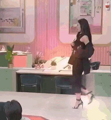 a woman in a black dress and high heels is walking in a room with a fire extinguisher on the wall .