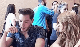 a man and a woman are sitting at a table in a room with a crowd of people .