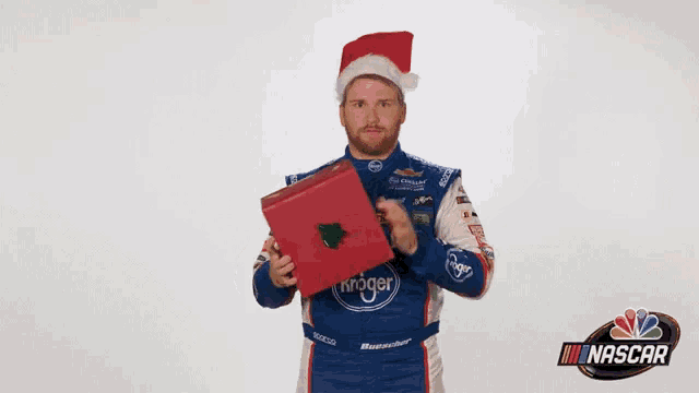 a man wearing a santa hat is holding a kroger gift box .