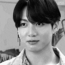 a black and white photo of a young man with earrings on his ears .