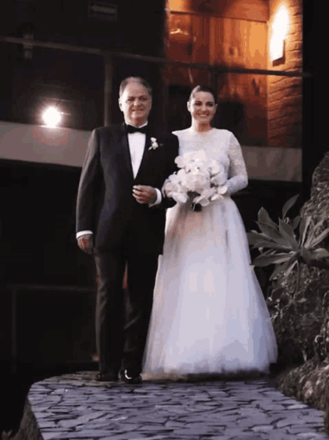a man in a tuxedo walks a woman in a white dress down a stone path