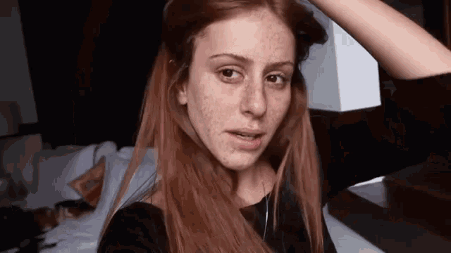 a woman with long red hair and freckles is looking at the camera while holding her hair .