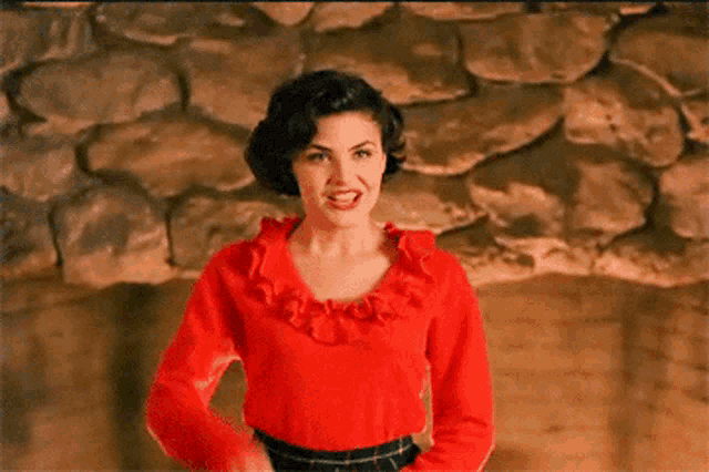 a woman in a red top and plaid skirt is pointing at the camera