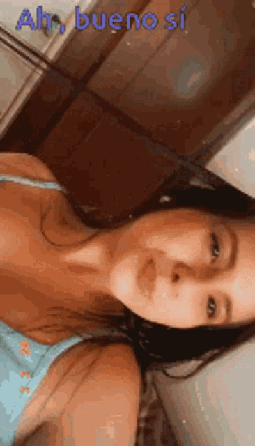 a woman in a blue tank top is taking a selfie with the words ah bueno si on the bottom