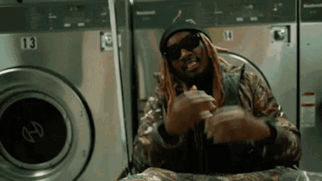 a man with long dreadlocks is sitting in front of a washing machine with the number 13 on it .
