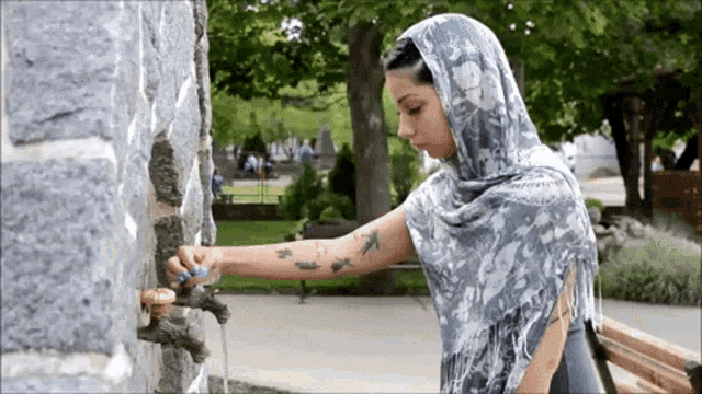 a woman with a scarf around her head is drinking water from a tap