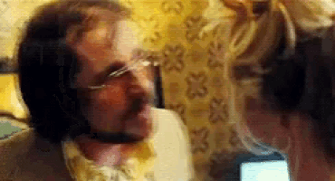 a man with glasses and a beard is talking on a cell phone with a woman .