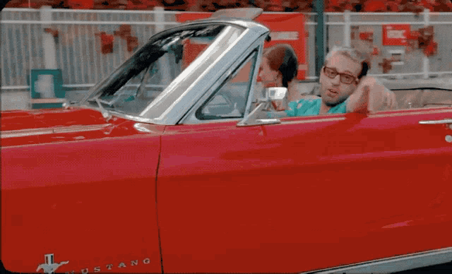 a man and woman in a red mustang car