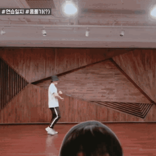 a man in a white shirt and black hat is dancing in a room with a wooden wall behind him