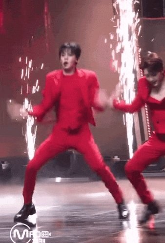a man in a red suit is dancing on a stage with fireworks in the background