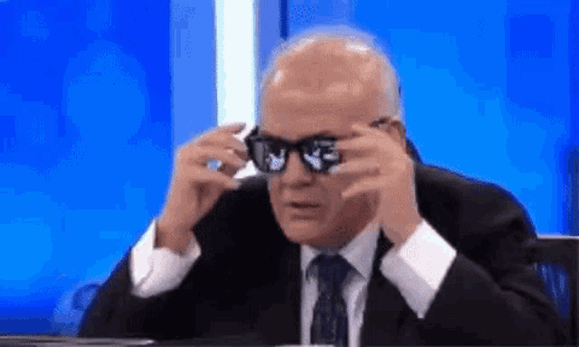 a man in a suit and tie is wearing sunglasses and looking through them .