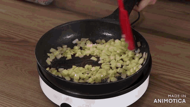 a pan of chopped onions is being stirred with a red spatula and the words made in animotica are visible