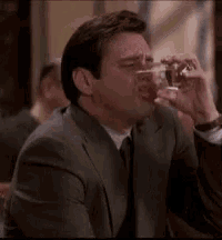 a man in a suit and tie is drinking water from a glass