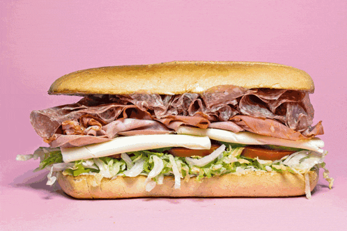 a sub sandwich with meat and cheese on a pink surface