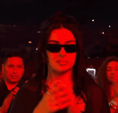 a woman wearing sunglasses is dancing in a crowd at a concert