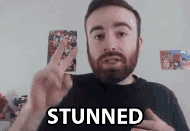 a man with a beard is giving a peace sign and the word stunned is on his chest .