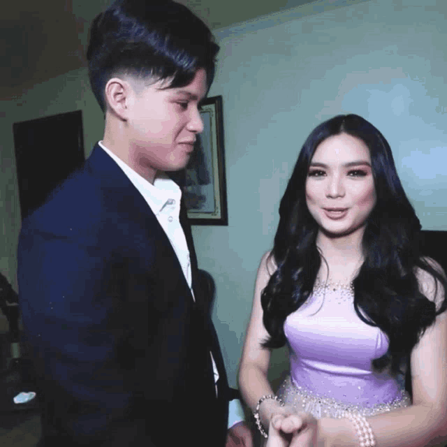 a man in a suit and a woman in a purple dress look at each other