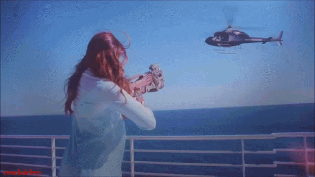 a woman is standing on a balcony looking at a helicopter flying over the ocean
