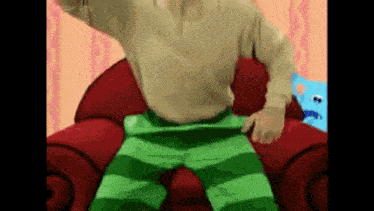a cartoon character is sitting on a red couch wearing green striped pants .