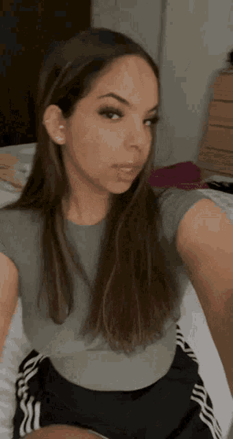 a woman is taking a selfie in a bedroom while wearing a grey shirt and black shorts .