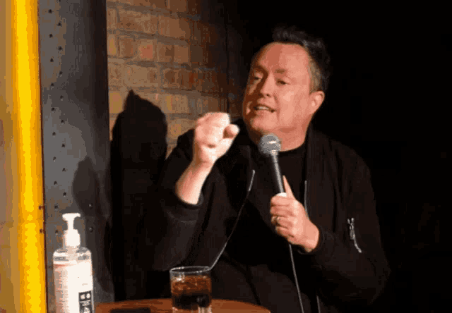 a man speaking into a microphone next to a hand sanitizer dispenser