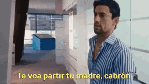 a man in a striped shirt is standing in a hallway with the words te voa partir tu madre cabron in yellow letters
