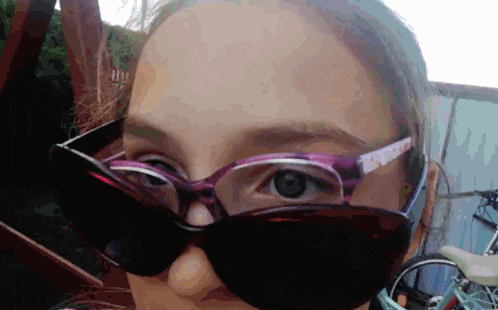 a woman wearing sunglasses and glasses looks at the camera