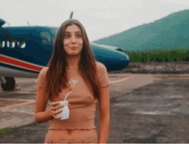 a woman is standing in front of a plane holding a cup