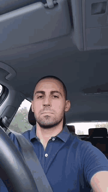 a man in a blue shirt is taking a selfie in a car