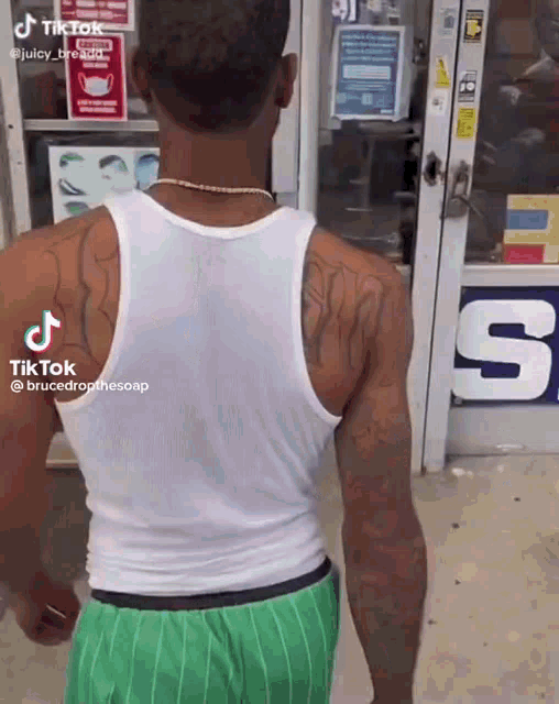 a man wearing a white tank top and green shorts is standing in front of a store door .