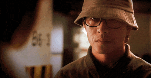 a man wearing glasses and a hat is standing in front of a sign that says bf 1