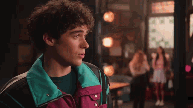 a young man with curly hair wearing a colorful jacket is standing in a room .