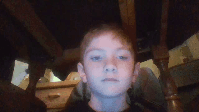 a young boy sits under a wooden table and looks at the camera