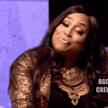 a woman wearing a gold jacket and a necklace with the word boo crew on the bottom