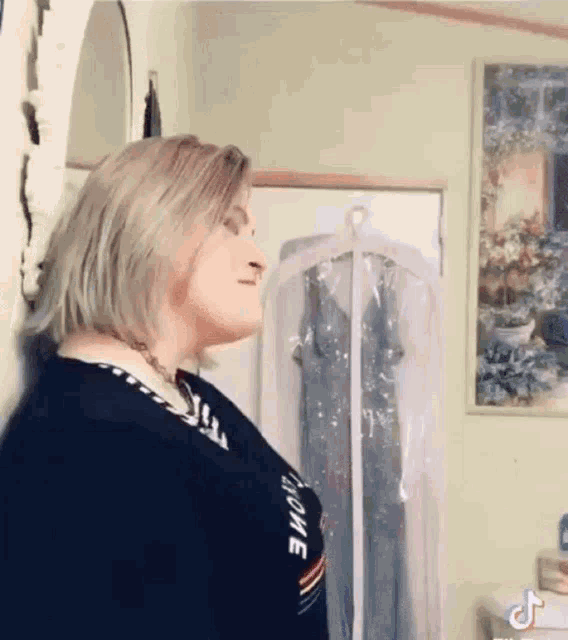a woman is leaning against a wall in a room next to a hanger with a dress on it .