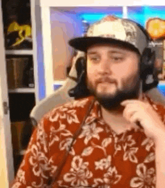 a man with a beard is wearing a hat and headphones while sitting in front of a computer .