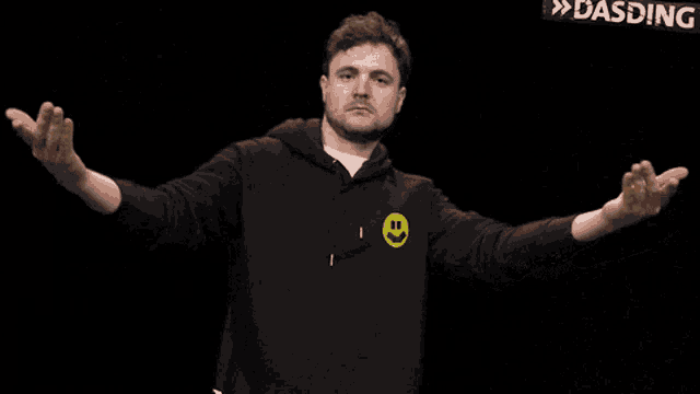 a man in a black hoodie with a yellow smiley face on the front