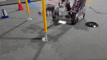 a purple robot is on a gray mat with a yellow stick in the middle