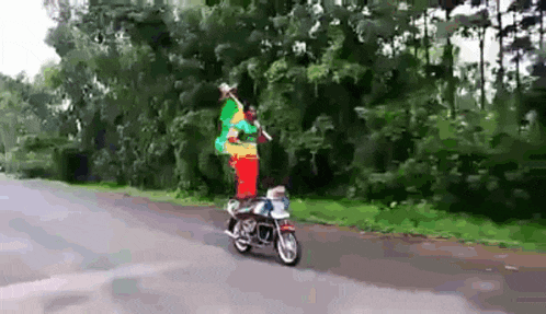 a man is riding a motorcycle down a road while holding a rasta flag .