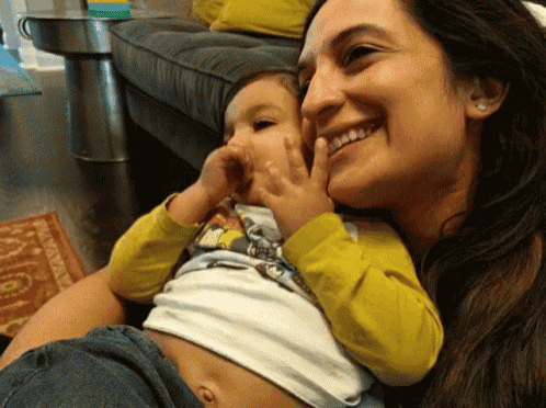 a woman is smiling while holding a baby in her lap and the baby is wearing a yellow shirt with a monkey on it