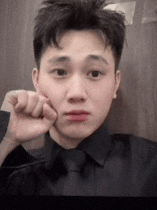 a young man in a black shirt and tie is taking a selfie with his hand to his face .