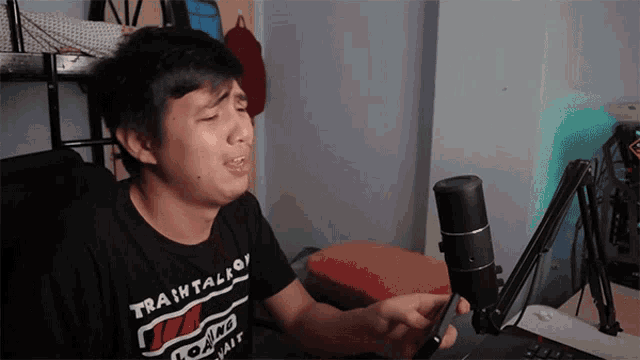 a young man singing into a microphone wearing a shirt that says train talk