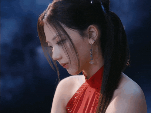 a woman wearing a red dress and earrings looks down at something